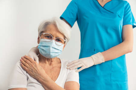 Slim unrecognizable female medical specialist supporting and holding an old lady with grey hair wearing a mask and glasses. High quality photoの写真素材