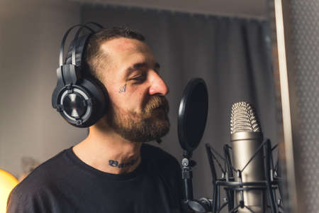 Tattooed caucasian middle-aged rap musician in studio recording his new song track. Closeup indoor shot. High quality photoの写真素材