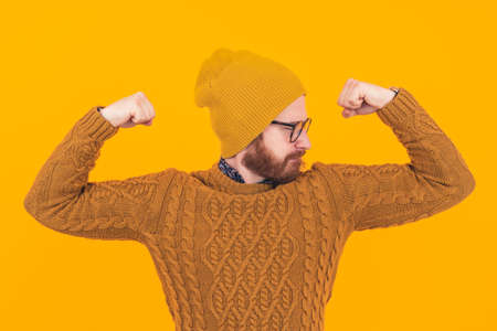 Fitness concept. Young caucasian millennial hipster man tightening both of his triceps and looking at one side over yellow background. High quality photoの写真素材