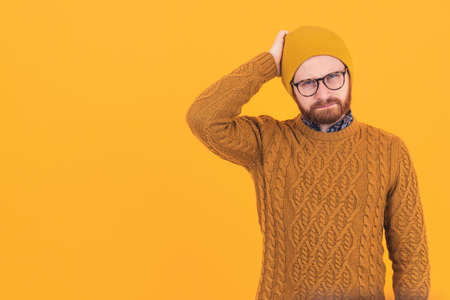 Confusion. Handsome bearded hipster in a beanie and knitted sweater touching his head and thinking...