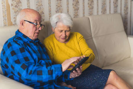 cute senior couple enjoying using mobile phone at home medium full shot indoor technology and seniority concept. High quality photoの写真素材