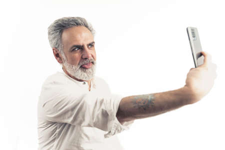 Medium studio shot on white background of an old good-looking funny man holding a mobilephone,...
