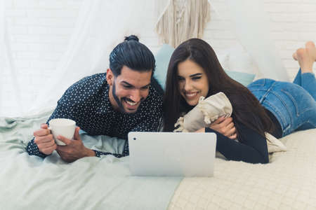 Young couple watching movies together on a laptop, spending free time together laying on the bed, rest after the hard day. High quality photoの写真素材