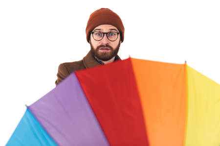 Studio portrait of a caucasian hipster man in autumn clothing including a beanie and a coat spinning his rainbow umbrella with a surprised facial expression. High quality photoの写真素材