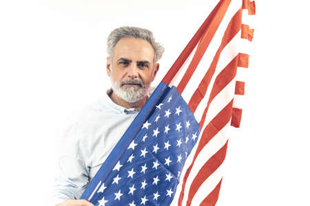 Proud American man in his 50s hiding behind the flag of United States of America. Portrait isolated on white background. High quality photoの写真素材