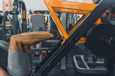 Close-up indoor shot of an unrecognizable caucasian man using a leg press. Man exercising in a modern gym. Healthy lifestyle concept. High quality photoの写真素材