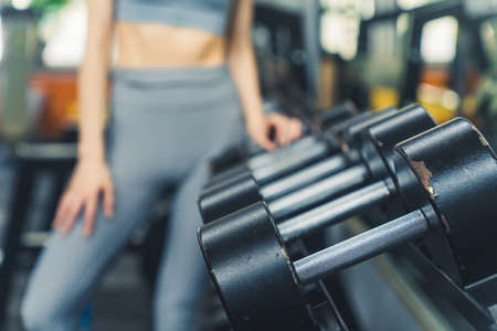 Close up of a blurred caucasian woman selecting one of black dumbbell weight at gym. Healthy lifestyle concept. High quality photoの写真素材