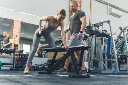 An attractive caucasian young adult woman using free weights at a fitness facility to build up her upper body strength under the guidance of her male private personal trainer. High quality photoの写真素材