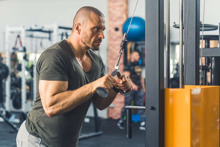 Bald caucasian well-built big guy focusing on exercise. Man holding a grip of a machine for pumping...