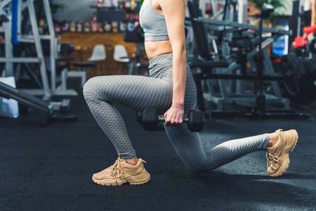 Lounge in bad position. Sporty Female Doing Deep Lunge Exercise Holding Two Dumbbells At The Gym. High quality photoの写真素材