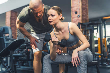 Healthy lifestyle concept. Gym interior. European muscular male bodybuilder trainer corrects the...