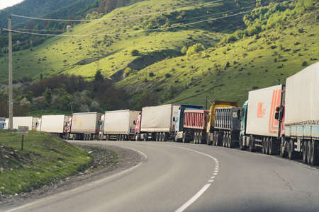 Long queue of trucks delivering products standing over picturesque mountain view. Contrast between nature and machines. Pollution concept. High quality photoの写真素材