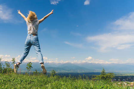 blond girl jumping on a beautiful view of a valley and Caucasus mountains in Georgia. full shot. High quality photoの写真素材