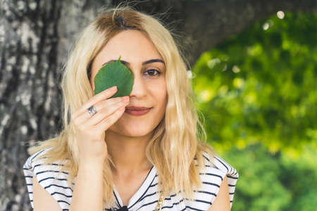 young blond Caucasian girl with a green leaf on the eye. medium closeup outdoor summer. High quality...