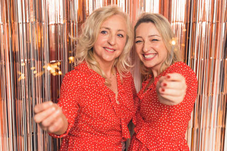 blonde Caucasian happy two women holding sparklers and celebrating New Year medium closeup indoors well being concept. High quality photoの写真素材