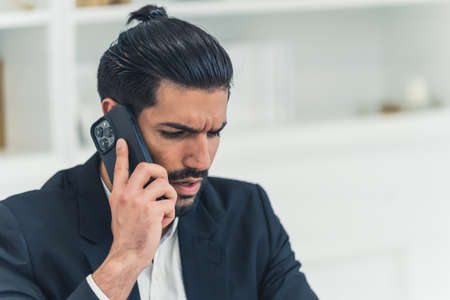 Annoyed combed handsome cuban man wearing a black suit and a white shirt talking on the phone, discussing business. High quality photoの写真素材