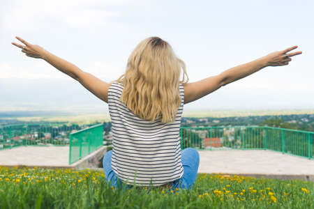 blond girl sitting on the grass and holding hands outstretched in the park. medium shot outdoor....