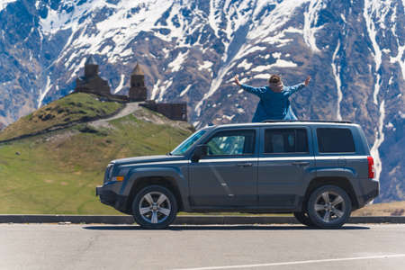 young woman sitting on the cars roof and enjoying the stunning view of Gergeti Trinity church, Kazbegi, Georgia. High quality photoの写真素材
