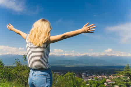 blond girl holding hands outstretched and enjoying a beautiful view of mountains and a valley. cowboy shot. High quality photoの写真素材