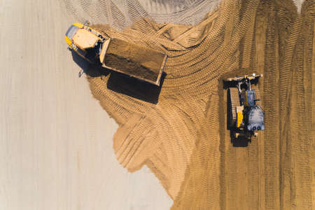 Aerial outdoor view of a tipper truck loaded with a pile of sand and a bulldozer moving the sand making track marks in the sand. High quality photoの写真素材