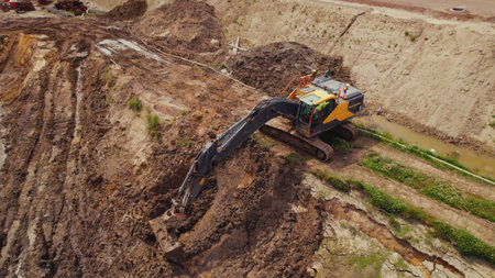 A yellow and black industrial machine digging a hole in a brown sand during works at a construction site. High quality photoの写真素材