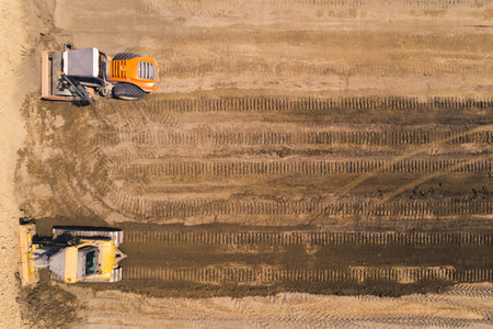 Road construction site of a new freeway. Two heavy industrial machines driving through loose sand,...