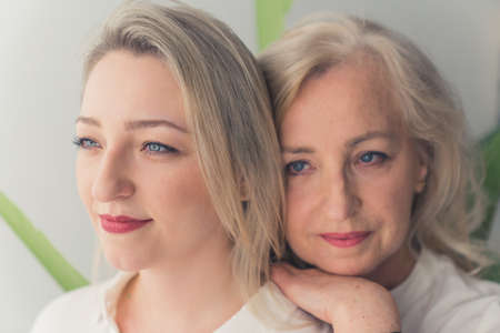 Close-up indoor shot of two blonde-haired beautiful millenial women with blue eyes wearing make-up, one woman leaning on the others shoulders. High quality photoの写真素材