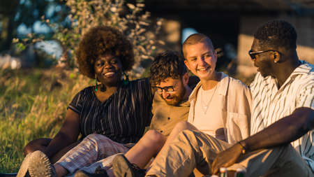 Group of happy young people having a weekend picnic in nature, sitting together on the grass near...