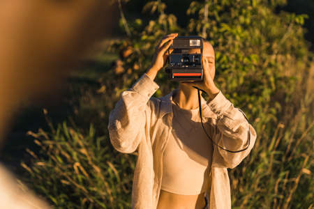 A young girl taking photos of her friend with an instant vintage camera. Weekend in nature at the...