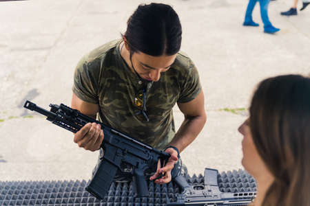 Handsome dark-haired muscular adult caucasian man in a moro t-shirt looking at a black gun at the resellers place. Outdoor shot. High quality photoの写真素材