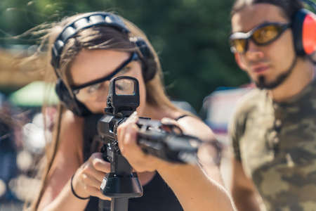 Strong long-haired caucasian girl pursuing her hobby by shooting from a black rifle with collimator....