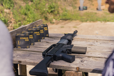 08.07.2022 Warsaw, Poland. Massive black shotgun on a wooden table next to five packages with...