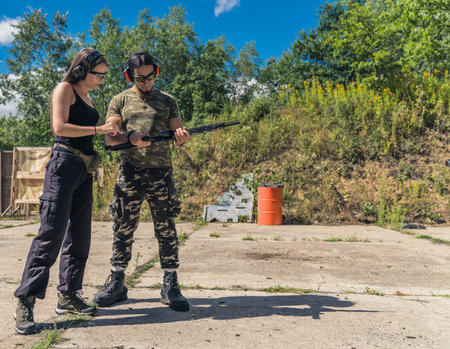 Full length outdoor shot. Private shooting lessons with instructor. Two people - caucasian man and woman - in military-like clothing in protective earphones. High quality photoの写真素材