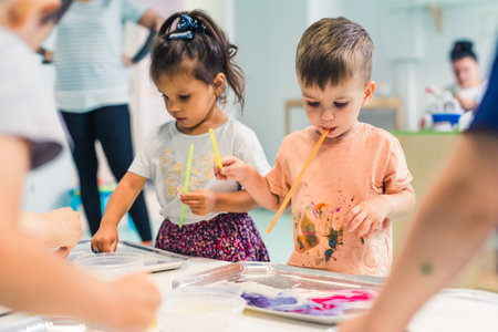 Multi-ethnic group of toddlers milk painting with the teacher helping them, using food coloring for colors. Children finger painting at the nursery school class. High quality photoの写真素材