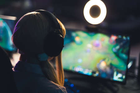 Unrecognisable teenage girl wearing headphones playing an online game on wide screen with ring...