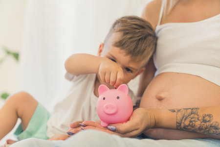 little cute Caucasian boy putting money in the piggy bank with his pregnant mom. High quality photoの写真素材