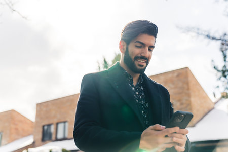 Horizontal outdoor shot. Latin sexy well-dressed man in his 20s standing near a street, messaging on his smartphone. High quality photoの写真素材