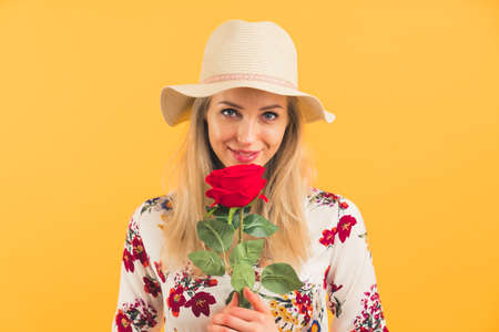Young white woman with long hair wearing straw hat and blouse holding rose below face smiling and looking invitingly at camera. Studio shot. High quality photoの写真素材