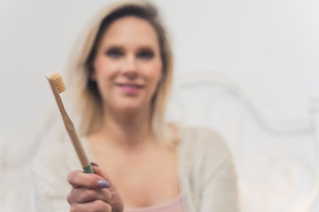Indoor portrait of an eco bamboo toothbrush held by a blurred unrecognizable blond caucasian woman. Oral healthcare concept. High quality photoの写真素材