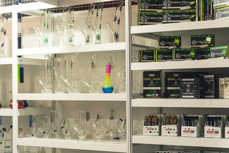 05.28.2022 Warsaw, Poland. White shop shelf full of medical cannabis related products. Rolled joints of CBD CBG marijuana, and glass bongs in various sizes and shapes. High quality photoのeditorial素材