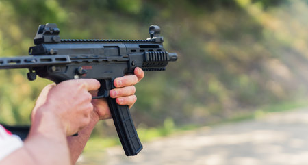 Hands holding submachine gun during training on shooting range. Blurred background. Outdoor...