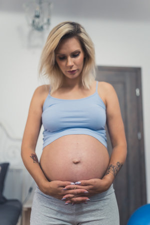 vertical medium shot of a blond pregnant woman at home. High quality photo