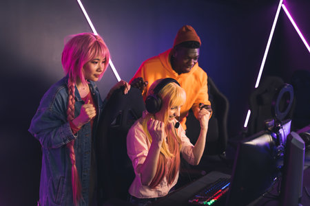 Happy young multiracial people having fun. Female caucasian player sitting on the gaming chair, her friends supporting her and jumping from happiness after her win. High quality photoの写真素材