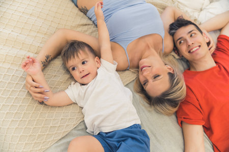 Cute family of three - mother, father, and their son - laying down together on a bed on their backs, laughing, enjoying their free time. High quality photoの写真素材