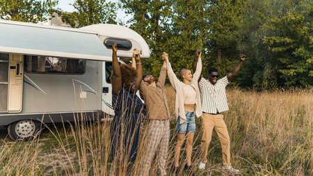 Group of happy young best friends, standing in nature, raising and holding each others hands after...