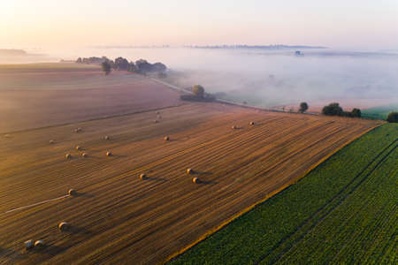 Birdseye view of green and golden fields with hay bales and trees. Sunrise over foggy landscape in Roztocze Poland. Horizontal shot. High quality photoの写真素材