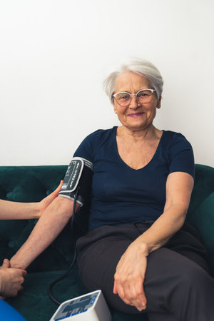 A pretty old woman, with short grey hair and her glasses on, sitting on the sofa and having her...