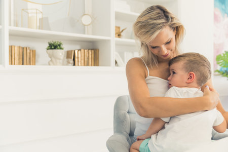 Mother and son. Modern living room interior. Beautiful young adult caucasian woman hugging her cute sleepy son. Time for a nap. High quality photoの写真素材