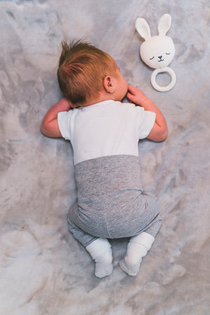 Newborn baby boy with cute brown hair, sleeping on his stomach on a blanket at home with his fluffy...