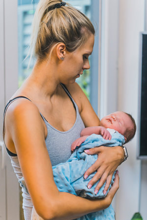 Caucasian married woman holding her newborn baby boy wrapped in a blanket, putting him to sleep